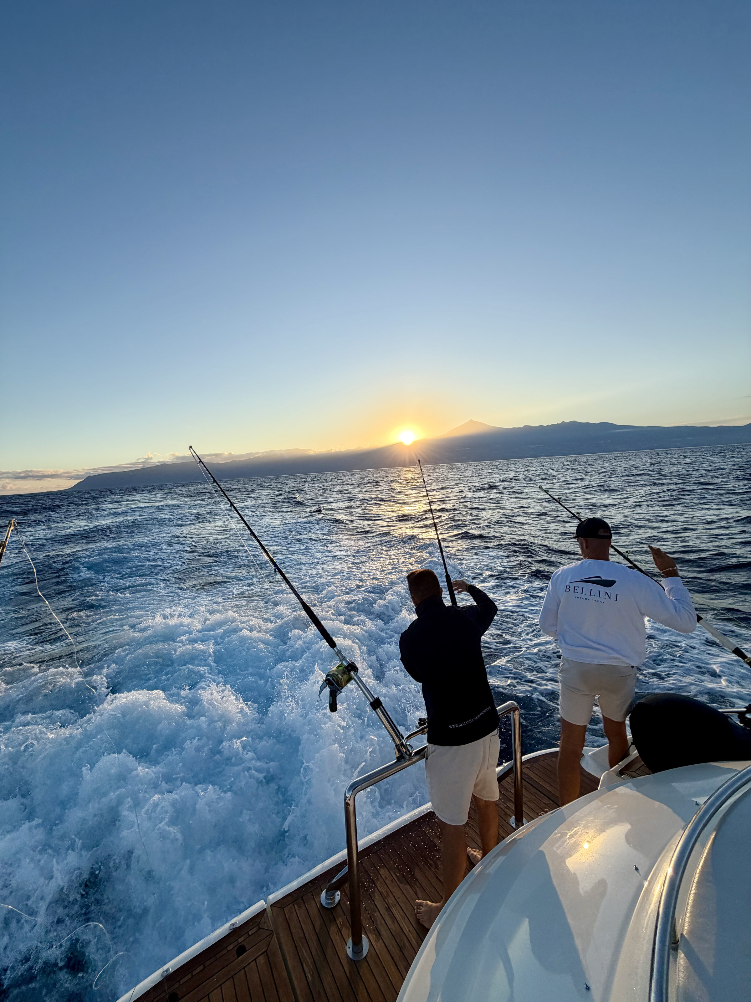 Dos personas pescando desde la popa al atardecer, de espaldas